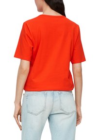 Rode katoenen T-shirt met een ronde hals en korte mouwen. Gecombineerd met lichtblauwe denim jeans met achterzakken en een relaxte pasvorm.
