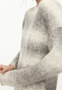 Pull rayé gris et blanc avec une coupe décontractée, texture tricotée et manches longues. Le matériau semble doux et confortable.