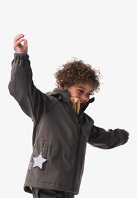Graue Zip-Jacke mit einem Stern-Detail auf der Tasche, ausgestattet mit elastischen Bündchen und einem weichen Innenfutter in einer kontrastierenden Farbe.