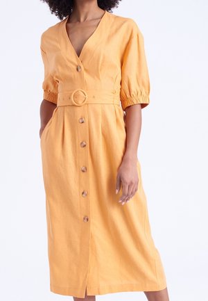 Robe en lin orange avec un col en V, des manches courtes bouffantes, une taille ceinturée et des boutons sur le devant qui descendent jusqu'à la jupe.