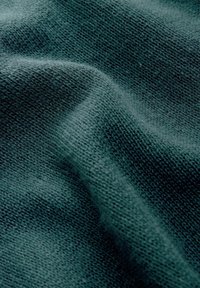 Zachte, donker teal gebreide stof met fijne textuur, close-up getoond, met kleine breisteekdetails en zachte plooien.