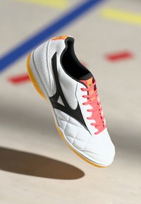 White athletic shoe with a quilted texture, black accents, and pink laces, featuring a yellow sole and a mesh panel on the upper.