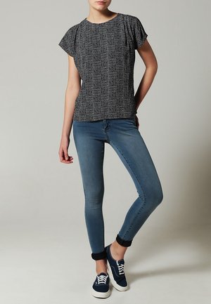 Camiseta negra con estampado y manga corta, combinada con unos vaqueros ajustados azul claro y zapatillas náuticas azul marino con suelas blancas, que llevan los puños doblados.