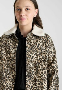Leopardprint spijkerjack met een crèmekleurige nepbontkraag, voorzien van knoopsluitingen en twee voorke pockets, op een model tegen een lichte achtergrond.