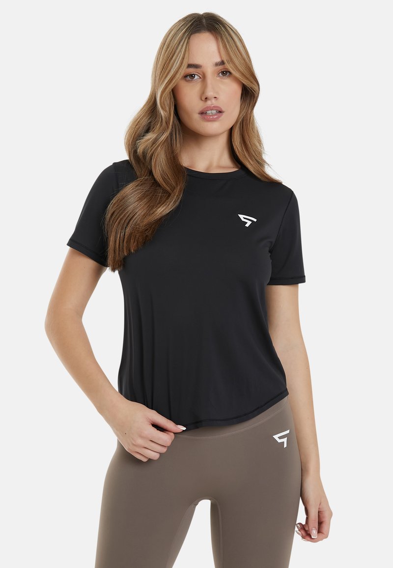 Črno športno majico s kratkimi rokavi, izdelano iz gladke tkanine. Bela zaščitna oznaka na levem prsnem delu. Združena z visokim bež leggingi.