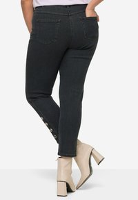 Donkerblauwe skinny jeans met twee achterzakken en knoopdetails bij de enkel. Draag met lichtgekleurde hakken.