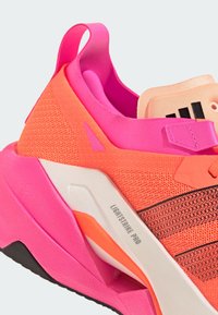 Sportsschuh mit leuchtend orangefarbener und pinker Mesh-Oberfläche, schwarzen Akzenten, strukturierten Details und einer dicken weißen Zwischensohle, die mit „LIGHTSTRIKE PRO“ gekennzeichnet ist.