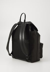 Sac à dos noir en tissu texturé et cuir lisse, avec des bretelles réglables, une poignée supérieure et une poche latérale.