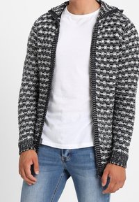 Cardigan lavorato a maglia in bianco e nero, con cappuccio, apertura frontale e polsini a coste. Texture morbida con motivo geometrico.