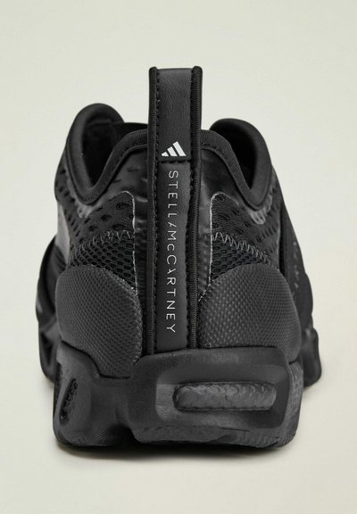 Black athletic sneakers made of mesh and rubber, featuring a high back, textured accents, and a branded pull tab with "STELL McCARTNEY."