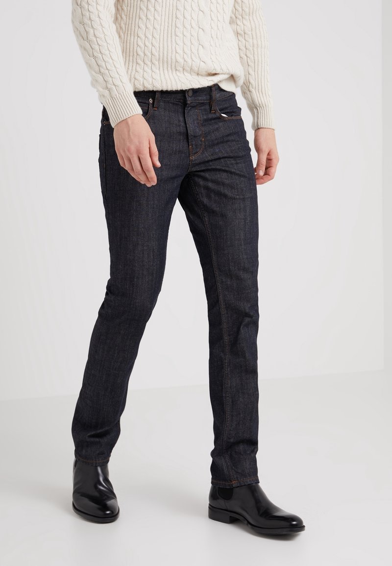 Mörkblå denimjeans med slim fit, med en klassisk fem-ficksdesign och kontrasterande sömmar, som bärs med svarta polerade kängor.