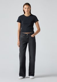Black cropped T-shirt paired with high-waisted, loose-fit black jeans. Model wears white sneakers; minimal design and no visible patterns.