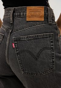 Εγγύς πλάνο της τσέπης παντελονιού Levi's σε σκούρο γκρι, με κόκκινη ετ�ικέτα Levi's και καφέ δερμάτινη ετικέτα με το λογότυπο στη μέση της μέσης.