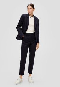 Marineblazer met gekleurde revers, witte top met zwarte accenten, op maat gemaakte broek en witte sneakers. Gladde textuur en moderne pasvorm.