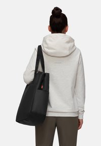 Sac fourre-tout noir avec design à double anse et une poche latérale, fabriqué dans un matériau lisse, associé à un sweat à capuche gris clair.