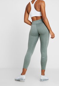 Gröna leggings med strukturerad yta, hög midja och meshdetaljer, tillsammans med vita träningsskor.