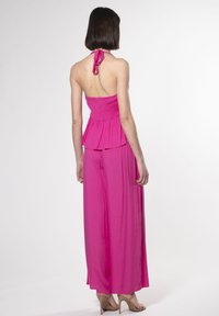 Roze halter jumpsuit met gerimpelde buste, uitlopende benen en peplumdetail. Gladde stof met een lichte, vloeiende textuur.