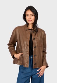 Giacca di pelle marrone con colletto, bottoni frontali e tasca sul petto; abbinata a pantaloni blu a vita alta.