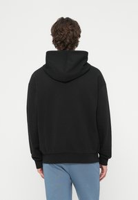 Čierna kapucňová mikina s voľným strihom, dlhými rukávmi a prúžkovanými manžetami. Hladká textúra; obsahuje klokaní vrecko a spevnené švy.