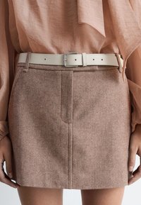 Brauner Fischgrätrock mit Vordernahtdetails, ausgestattet mit einem beigen Leder-Gürtel und einer silbernen Schnalle. Strukturierter Stoff mit tailliertem Design.