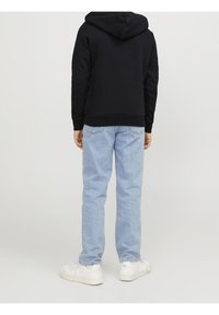 Felpa nera con cappuccio, jeans azzurri chiari e sneakers bianche. La felpa ha polsini e orlo costolati; i jeans presentano tasche posteriori e leggero effetto usato.