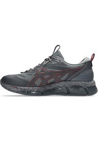 Scarpa sportiva grigia con accenti rossi, sovrapposizioni testurizzate e un sottopiede maculato. Caratterizza una punta arrotondata e una suola ammortizzata per il supporto.