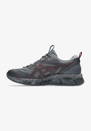Gray athletic shoe with red accents, textured overlays, and a speckled midsole. Features a rounded toe and cushioned sole for support.