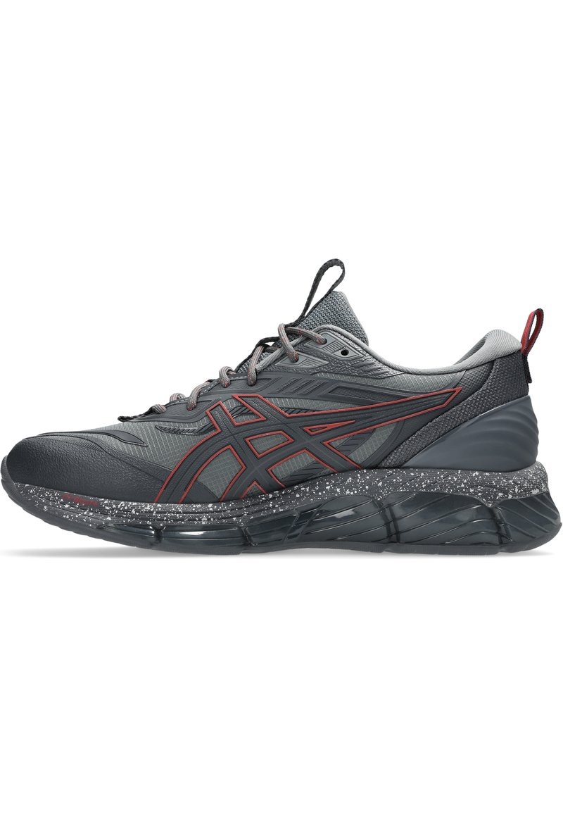 Scarpa sportiva grigia con accenti rossi, sovrapposizioni testurizzate e un sottopiede maculato. Caratterizza una punta arrotondata e una suola ammortizzata per il supporto.