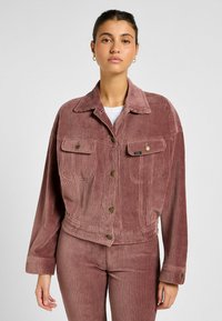 Giacca di velluto a coste in rosa polveroso, con tasche sul petto, bottoni dorati e un design cropped con maniche ampie. Strisce verticali testurizzate.