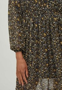 Blommig klänning med mörk bakgrund, prydd med gula, blå och vita blommor. Halvgenomskinligt tyg, rynkad midja och puffärmar.