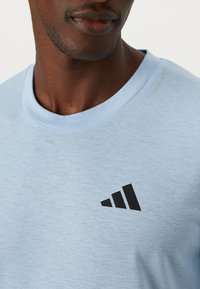 Lichtblauw t-shirt van zacht materiaal, met een zwart Adidas-logo op de borst. Ronde halslijn met gestikte randen.