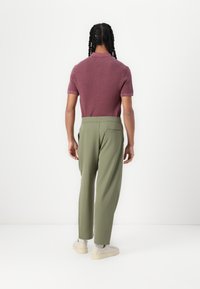 Bordo polo majica kratkih rukava s teksturiranim materijalom, u kombinaciji s maslinasto zelenim suknjažnim hlačama s elastičnom strukom i stražnjim džepom.