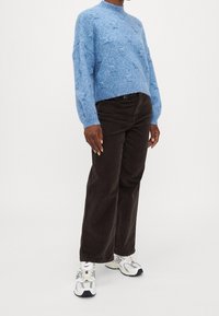 Suéter azul texturizado con un cuello alto, combinado con pantalones de pana marrón oscuro y zapatillas blancas con acentos en gris y negro.