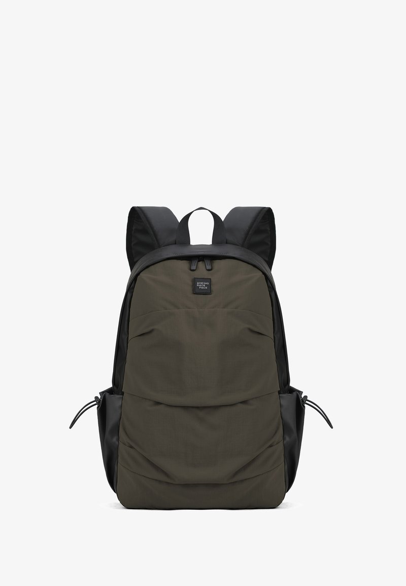 Sac à dos avec un corps en tissu vert olive mat et des accents noirs. Il dispose de bretelles rembourrées et d'une poignée de transport supérieure. Poche zippée à l'avant.