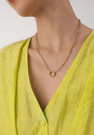 Gold chain necklace with a circular pendant worn on a person’s neck, paired with a bright yellow buttoned garment.