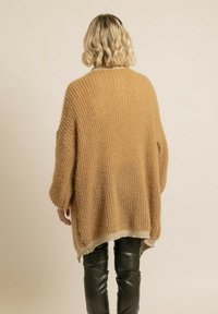 Pull en maille de couleur brun clair, design oversized avec une texture côtelée et un ourlet bicolore. Assorti à un pantalon en simili cuir noir ajusté.