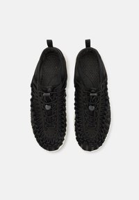 Zwarte geweven slip-on schoenen met verstelbare bungee veters en gestructureerde binnenzolen, gezien van boven op een witte achtergrond.