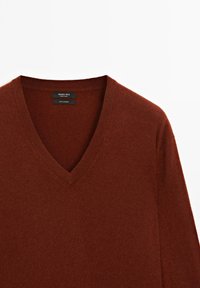 Maglione in cashmere a V in un caldo colore ruggine, con collo a costine e una consistenza morbida. Etichetta che indica "Massimo Dutti, 100% cashmere."