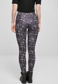 Sorte leggings med et himmelsk mønster av måner, stjerner og planeter i hvitt. Stoffet har en glatt, elastisk tekstur.