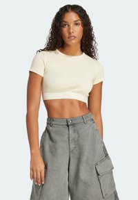 Kreemist ribiga lühikeste varrukatega crop top, millel on valge logo riba; kombineeritud laia halli cargo pükse, millel on küljetaskud ja nupuga sulgemine.