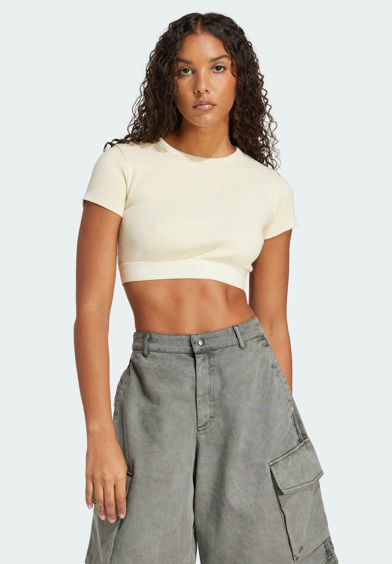 Kreemist ribiga lühikeste varrukatega crop top, millel on valge logo riba; kombineeritud laia halli cargo pükse, millel on küljetaskud ja nupuga sulgemine.