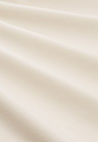 Crème-kleurige katoenstof met een gladde textuur, voorzien van subtiele plooien en een consistente, zachte uitstraling.