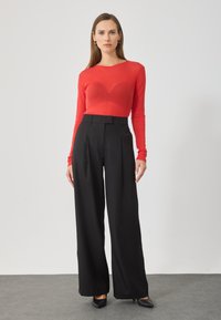 Top roșu cu mânecă lungă din material transparent, cu decolteu în formă de barcă, asociat cu pantaloni negri cu talie înaltă, cu picioare late, prezintă pliseuri și buzunare laterale.