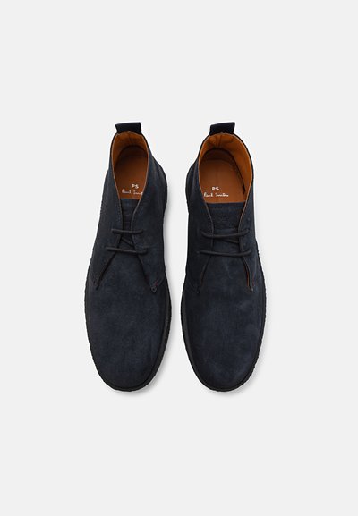 Botas chukka de ante azul oscuro con punta redonda, diseño de cordones, forro de cuero y detalles de costura a lo largo de la suela.