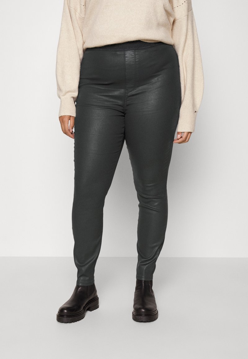 Leggings en similicuir vert avec une taille haute, présentant une texture lisse et une coupe ajustée, associés à des bottines noires épaisses.