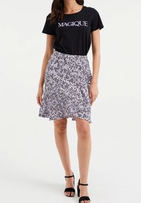 Černé tričko s textem "MAGIQUE", ve spojení s lilkovou sukní s vzorem a volným lemem. Oblečeno s černými sandály na podpatku.