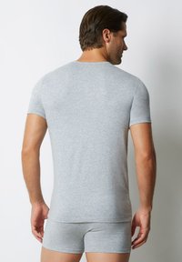 T-shirt grigio a maniche corte realizzato in tessuto morbido, design aderente, con collo rotondo e texture liscia, indossato con pantaloni boxer coordinati.