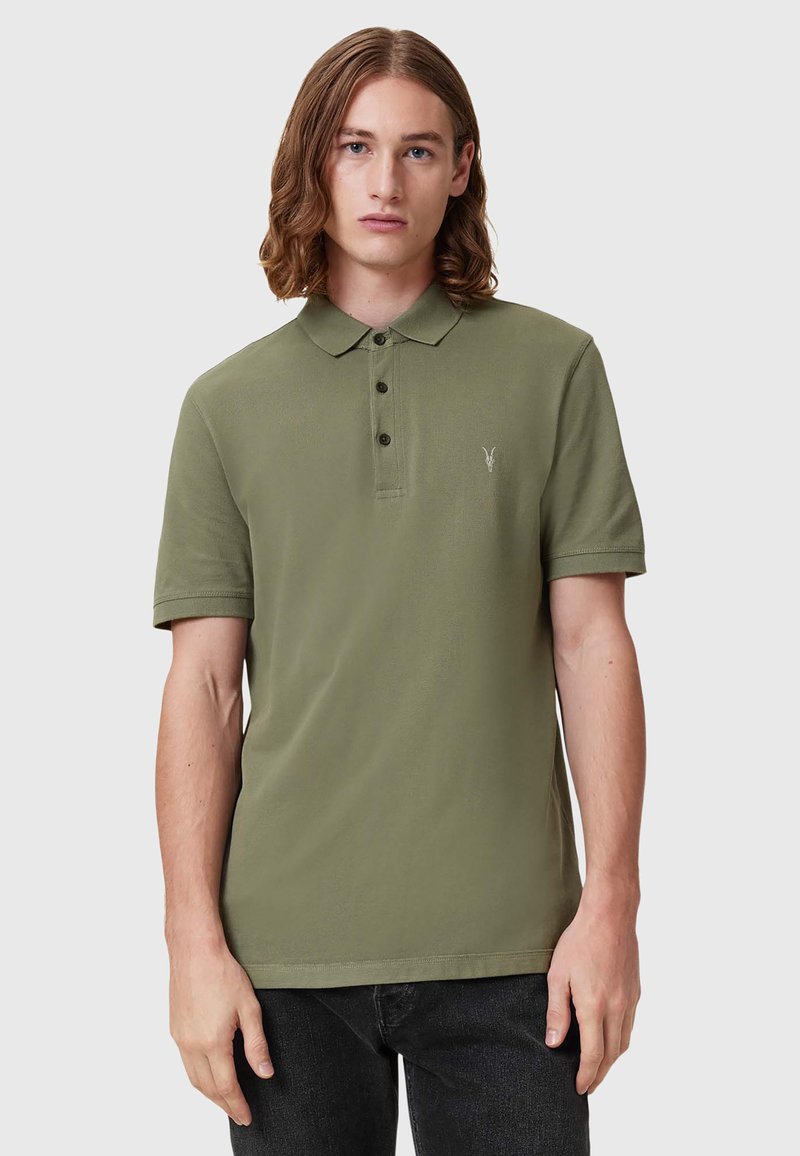 Olivenfarget polo skjorte med flat krage, tre knappelukkinger og en liten brodert logo. Stoffet er glatt og lett.
