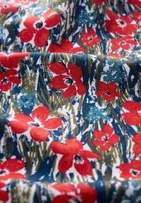 Tissu en coton avec un fond bleu orné de fleurs rouges, de feuilles vertes et de textures abstraites. Le design a un style pictural.