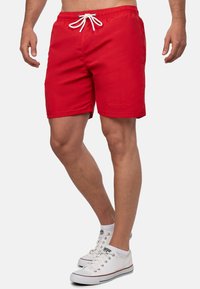 Pantaloni da nuoto rossi con vita elastica, cordoncino bianco e orlo arrotondato. Presentano un logo sottile ricamato sul davanti.